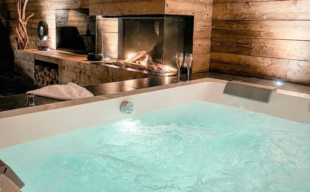 Balnéo Jacuzzi double en eau face à la cheminée allumée dans la suite La Chaleureuse